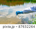 Analysis, water sample from the river, lake. A gloved hand collects water in a test tube. 87632264