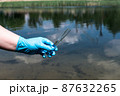 Analysis, water sample from the river, lake. A gloved hand collects water in a test tube. 87632265
