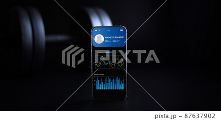 Fitness app. Smart phone screen with fitness health or sport gym mobile application on black dumbbell background. App for training indoors. Fitness app. Smart phone screen with fitness health or sport gym mobile application on black dumbbell background. App for training indoors. 87637902