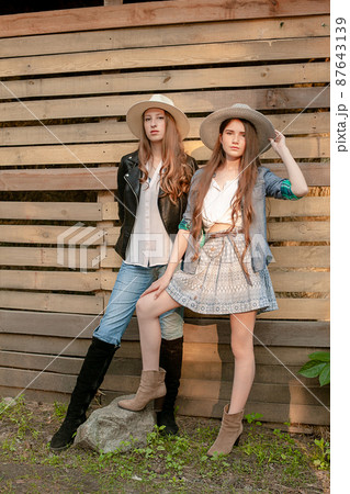 Two teen girls in rustic style clothes and wide-brimmed hats posing on wooden boards background 87643139