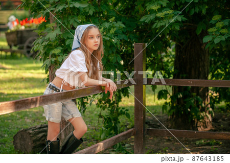 Dreamy tween girl standing near animal stall in summer country estate 87643185