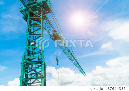 Green hoisting crane on blue sky background with clouds, close up of The Tower Crane. The construction crane with the cloud sky background at the construction site. The Tower Crane against a blue sky. Green hoisting crane on blue sky background with clouds, close up of The Tower Crane. The construction crane with the cloud sky background at the construction site. The Tower Crane against a blue sky. 87644385