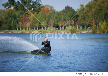 Wakeboarder surfing on lake. Young man surfer having fun wakeboarding in the cable park. Water sport, outdoor activity concept. 87647049