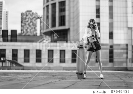 Woman on a skateboard in the city. Beautiful contrasting black and white photo of a woman riding around the city. 87649455