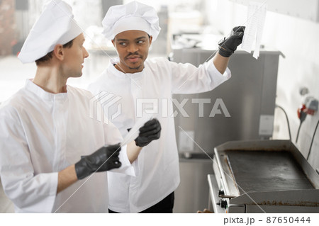Chefs look on printed checks with orders while cooking in the professional kitchen Chefs look on printed checks with orders while cooking in the professional kitchen 87650444