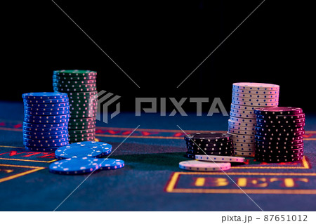 Colorful chips piles standing on blue cover of playing table. Black background. Gambling entertainment, poker, casino concept. Close-up. Colorful chips piles standing on blue cover of playing table. Black background. Gambling entertainment, poker, casino concept. Close-up. 87651012