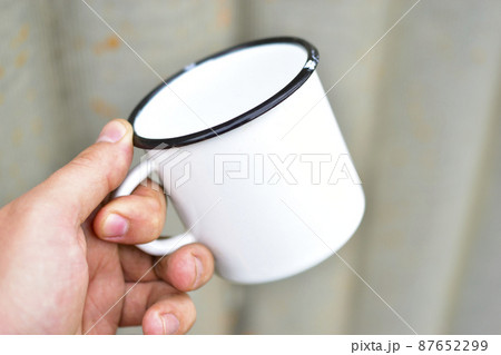 White metal enameled mug in the hands of a person 87652299