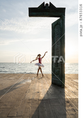 Female ballet dancer is posing near art object on seafront during sunrise Female ballet dancer is posing near art object on seafront during sunrise 87653316
