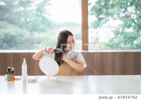 ヘアブラシで髪をとかす女性（笑顔） 87654792