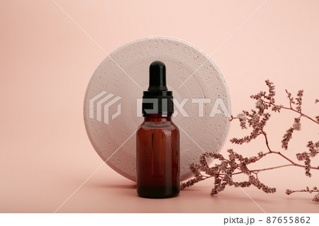 Skin serum or oil in dark brown glass bottle with round gypsum circle and dry flower against beige background 87655862