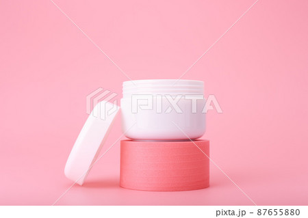 Opened cosmetic jar on pink pedestal against bright pink background. Concept of luxury repairing nourishing cream  87655880