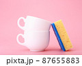 Creative, minimal dishwashing concept, yellow cleaning sponge next to two white ceramic cups on pink background 87655883