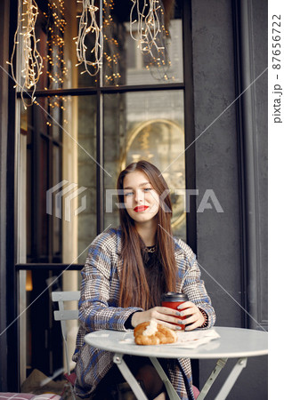 Girl with red lips sitting in a cafe outdoors and drinking coffee Girl with red lips sitting in a cafe outdoors and drinking coffee 87656722
