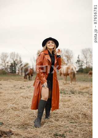 Beautiful blonde woman standing in the field with horses 87656781