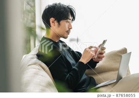 家のソファーでスマホを見る男性 87658055