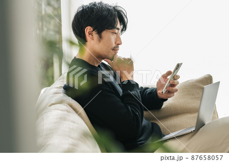 家のソファーでスマホを見る男性 87658057
