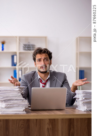 Young male employee unhappy with excessive work in the office Young male employee unhappy with excessive work in the office 87660225