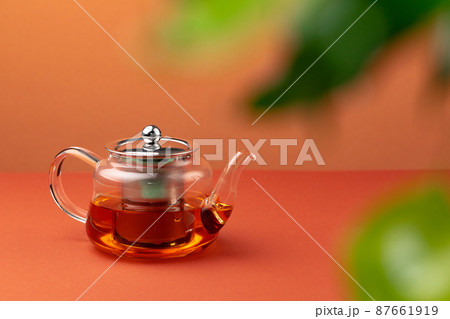 Glass teapot with black tea on background of blurred foliage 87661919