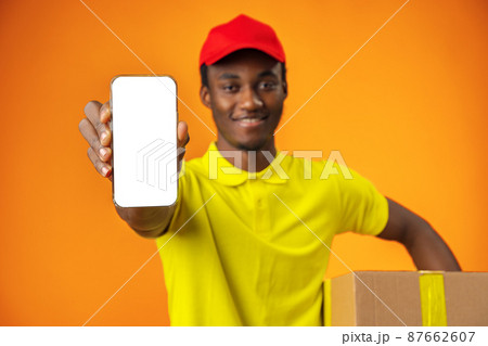 African courier guy showing smartphone with blank screen and holding box in studio 87662607
