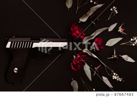 Flat lay for the world, on a black background gun and rose flowers, simulating a shot Flat lay for the world, on a black background gun and rose flowers, simulating a shot 87667483