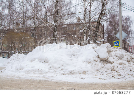 A huge large snowdrift by the road against the backdrop of city houses and trees A huge large snowdrift by the road against the backdrop of city houses and trees 87668277