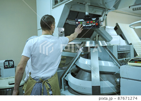 At the bakery: male baker regulating level of power on a control panel of a dough kneading machine At the bakery: male baker regulating level of power on a control panel of a dough kneading machine 87671274