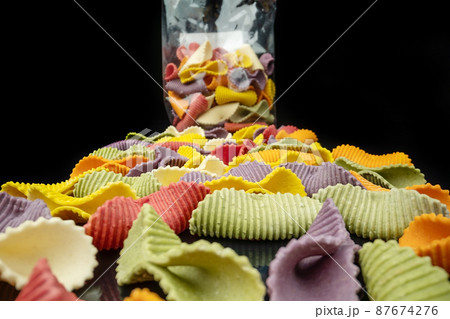 Creative multicolored pasta farfalle on a black background in perspective with packaging in the background. Extreme macro 87674276