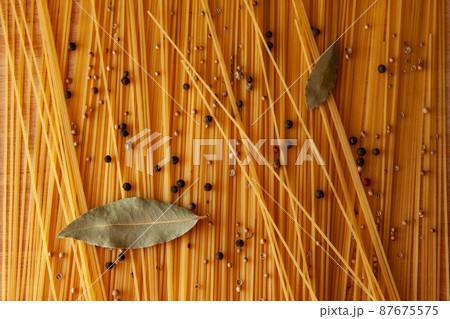 Food theme: raw pasta as whole background. Yellow Spaghetti scattered on the table with black pepper peas for publication, poster, calendar, post, screensaver, wallpaper, postcard, card, banner, cover 87675575