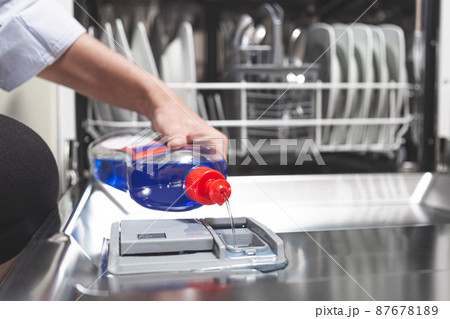 Close-up hand filling dishwasher with gloss liquid into the dishwasher box. Housework concept. Close-up hand filling dishwasher with gloss liquid into the dishwasher box. Housework concept. 87678189