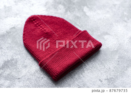 Red warm knitted women's hat on a concrete background 87679735