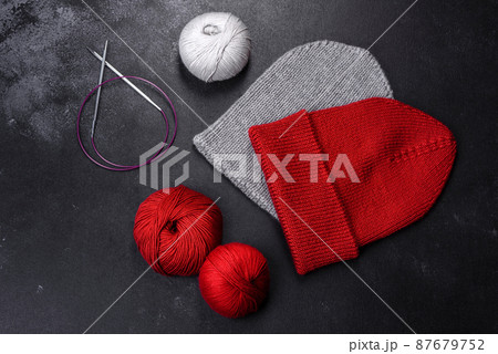 Red warm knitted women's hat on a concrete background 87679752