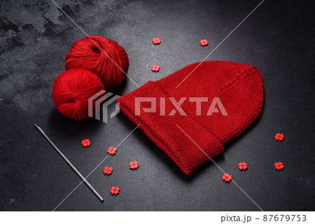 Red warm knitted women's hat on a concrete background 87679753