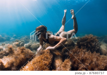 Young woman explore sea bottom with seaweed. Freediving and sun light in ocean Young woman explore sea bottom with seaweed. Freediving and sun light in ocean 87680737