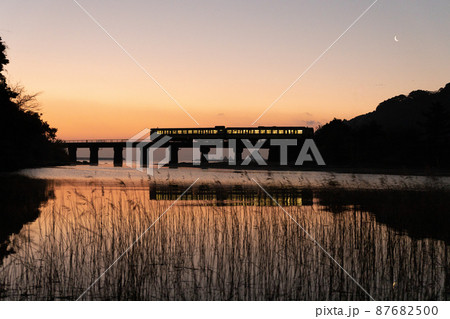 マジックアワーと共に昇る日出の宮崎県日南市山王の日南海岸山王浜を走るJR九州キハ40日南線通勤列車 87682500