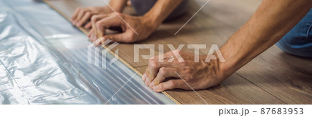 BANNER, LONG FORMAT Father and son installing new wooden laminate flooring on a warm film floor. Infrared floor heating system under laminate floor 87683953