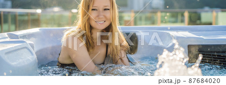BANNER, LONG FORMAT Portrait of young carefree happy smiling woman relaxing at hot tub during enjoying happy traveling moment vacation life against the background of green big mountains 87684020