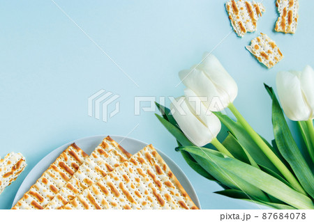 Happy Passover concept. Matzo and white tulips on a blue background. Religious Jewish holiday Pesach. Copy space, flat lay. Happy Passover concept. Matzo and white tulips on a blue background. Religious Jewish holiday Pesach. Copy space, flat lay. 87684078