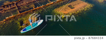 Woman on paddle board, sup next to Abandoned broken shipwreck sticking out of the sea BANNER, LONG FORMAT 87684334