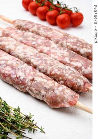 Minced and shaped lamb mutton kebabs, with grill ingredients, on white stone table background 87693043