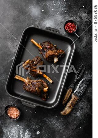 Slow Cooked Lamb Shanks meat, on black dark stone table background, top view flat lay Slow Cooked Lamb Shanks meat, on black dark stone table background, top view flat lay 87693086