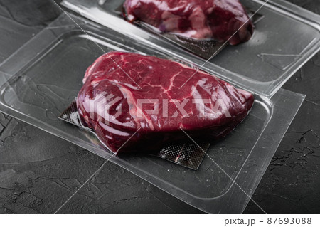 Market pack with raw rump beef steak, on black dark stone table background, with copy space for text 87693088