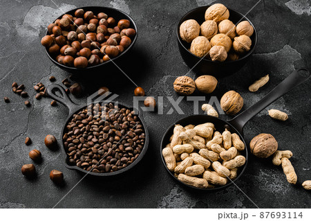 Assortment of nuts in shells, peanut, walnut, pine nuts and hazelnut, on black dark stone table background Assortment of nuts in shells, peanut, walnut, pine nuts and hazelnut, on black dark stone table background 87693114
