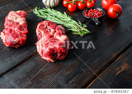 Organic raw chuck eye roll beef steak cut with rosemary red onin, garlic peppercorns and tomatoes on old dark wooden table. Side view with space for text. 87693267