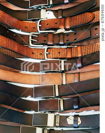 Various types of brown leather belt in a row for display and sale on the market. Realistic leather belts set with metal buckles. Clothing store, shelf with men's waist belts. Selective focus. 87694600