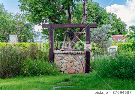 Beautiful artesian well made by stones and wheel pulley with metal bucket and rope in peaceful garden atmosphere. Retro stone water well in rural area. Garden decoration with antique items. 87694687
