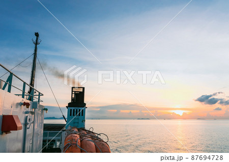 Scenery view of exhaust pipe of ferry boat with black thick smoke coming out and sky with clouds on background. Smoke from ferry boat flue during sea with sunlight, sea water. Air pollution. Scenery view of exhaust pipe of ferry boat with black thick smoke coming out and sky with clouds on background. Smoke from ferry boat flue during sea with sunlight, sea water. Air pollution. 87694728