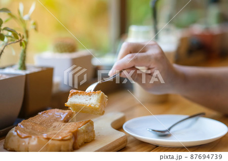 Close up to slices of toast bread and butter with steamed Thai tea custard topping in hand of woman using a fork to eat for breakfast. A hand eating delicious home made Thai tea Custard Toast dessert. Close up to slices of toast bread and butter with steamed Thai tea custard topping in hand of woman using a fork to eat for breakfast. A hand eating delicious home made Thai tea Custard Toast dessert. 87694739