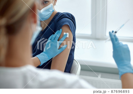 Woman in medical face mask getting injection at hospital. Doctor or nurse preparing syringe to give shot to female patient, concept of inoculation 87696893