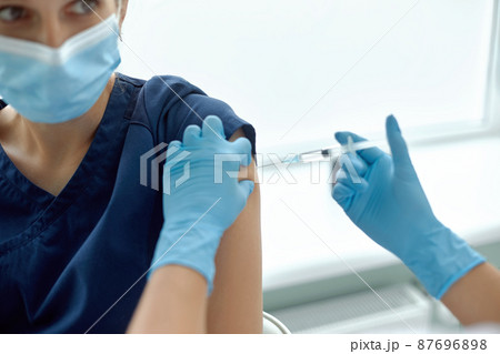 Woman in medical face mask getting injection at hospital. Doctor or nurse preparing syringe to give shot to female patient 87696898