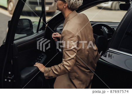 Woman Dressed in Rumpled Brown Jacket Getting of from the Car 87697574